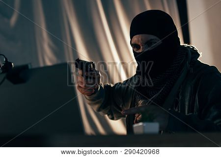 Aggressive Criminal In Mask Pointing With Finger And Aiming Gun At Laptop Screen