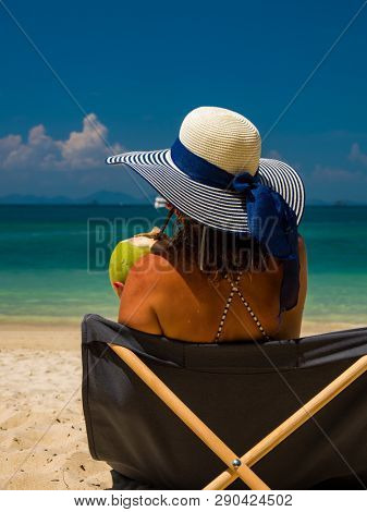 Woman with straw hat enjoying her holidays on a transat at the tropical beach in Thailand