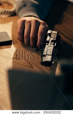 Cropped View Of Criminal Holding Gun On Wooden Table
