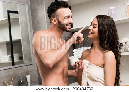 Cheerful Shirtless Boyfriend Applying Face Cream On Nose Of Brunette Girlfriend