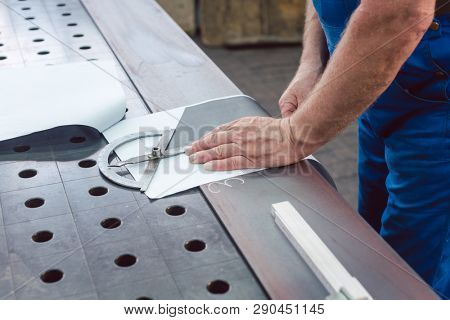 Metalworker with angle meter measuring strip of metal for later cutting