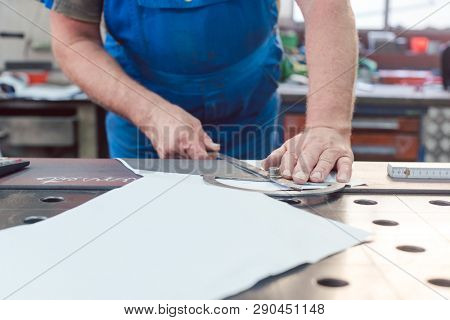 Metalworker with angle meter measuring strip of metal for later cutting