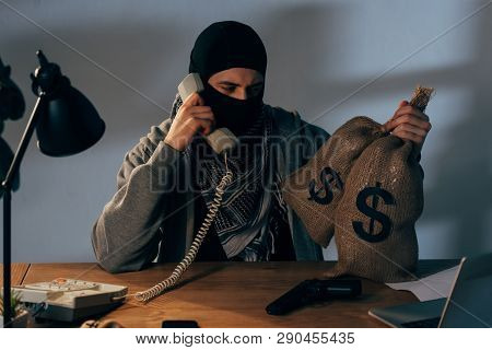 Terrorist In Mask Holding Bags With Money And Talking On Phone In Room
