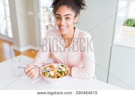 Young african american woman eating healthy pasta salad with a happy face standing and smiling with a confident smile showing teeth