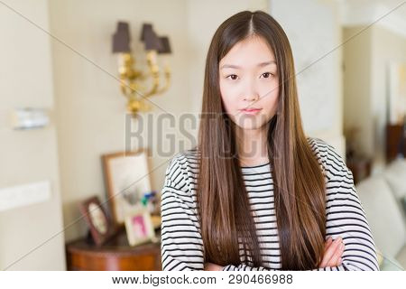 Beautiful Asian woman wearing stripes sweater over living room background Relaxed with serious expression on face. Simple and natural with crossed arms