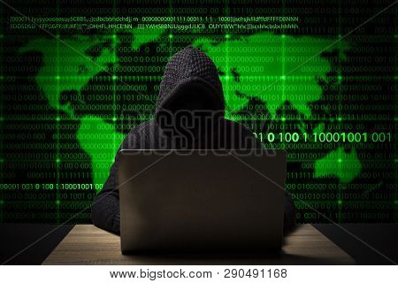 Hacker In A Jacket With A Hood With A Laptop Sits At The Table. Added Identity Theft Icons, Account 