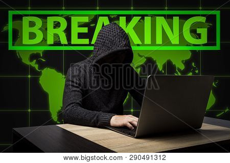 Faceless Man In A Hooded Robe Sits At A Table With A Laptop. Concept Of Hacking And Stealing User Da