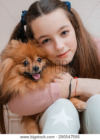 Teenage Girl With A Dog Breed Spitz Rejoices With A Pet At Home On The Floor. Care And Training Of A