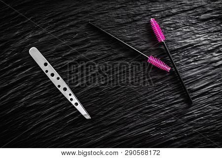 On The Black Background Lies A Pair Of Tweezers And Eyebrow Comb Brush The Top View Copy Space