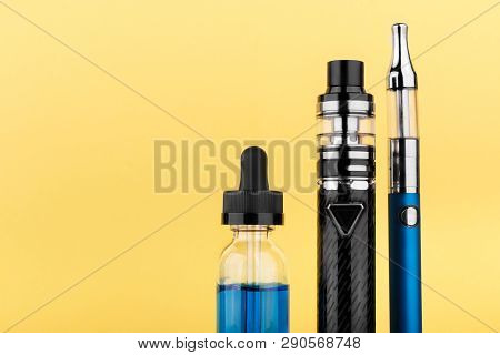 Vaping Device Collection And Bottle With Blue Vape Liquid On Yellow Background. Close Up