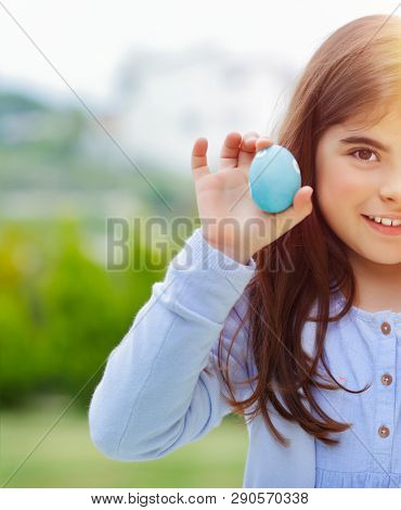 Portrait of a cute baby girl holding in hand blue decorated egg, amazing spring sunny day,  little eggs hunter, happy Easter egg hunt