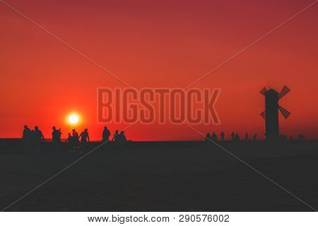 A Group Of People After A Hard Day Work Returns To The Mill, Against The Background Of The Sunset An