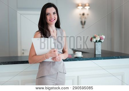 Portrait Of Elegant Middle Aged Woman Standing In Kitchen At Home Holding Papers In Her Hands