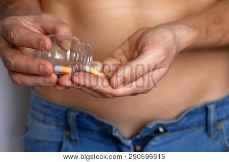 Man Taking Pills, Bottle With Capsules In Male Hands Close Up. Muscular Guy In Unzipped Jeans With N
