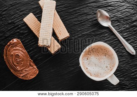 A Piece Of Bread, A Mug Of Coffee And A Waffle, Smeared With Chocolate Paste, On A Black Textured Ba