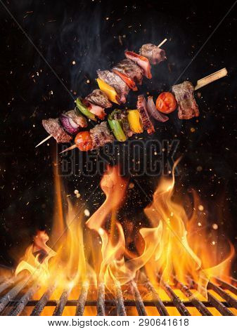 Tasty skewers flying above cast iron grate with fire flames. Freeze motion barbecue concept.