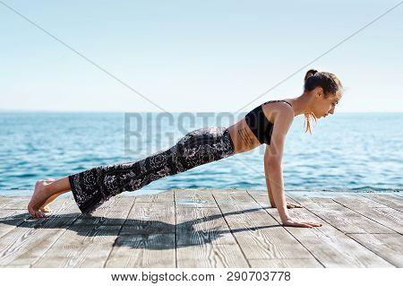Photo Of Young Sports Woman Make Yoga Exercises On The Beach With Sea Background. Feeling So Comfort