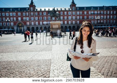 Visiting Famous Landmarks And Places.cheerful Female Traveler At Famous Plaza Mayor Square Reading A