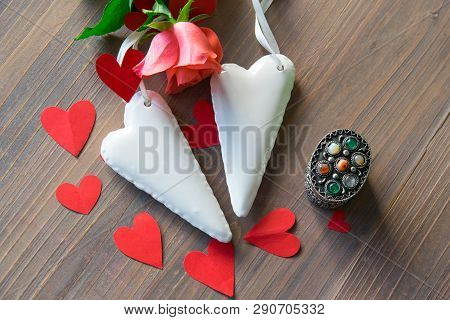 Two Porcelain White Hearts On The Wood Textural Table With Pink Flower And Many Red Paper Hearts Aro