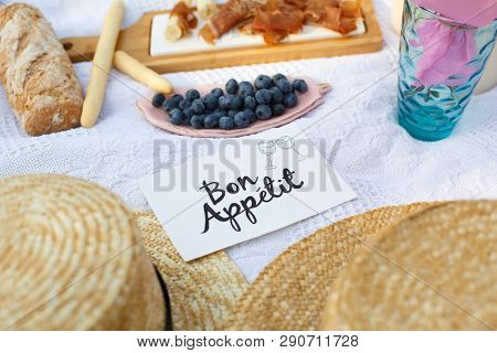 Straw Hats Lay On A White Picnic Blanket Next To Nameplate Bon Apetit Bright Summer Day Background. 