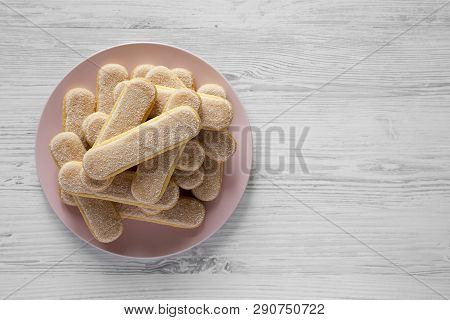Savoyardi Biscuits Or Ladyfingers Cookies On Pink Plate Over White Wooden Background, Top View. Flat