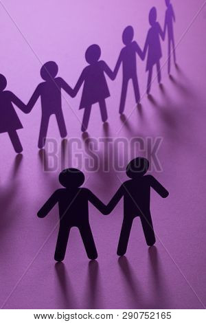 Black paper figure of male couple in front of a crowd of paper people holding hands on purple surface. Social movement, protest, minorities concept.