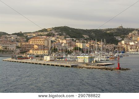 Isola Maddalena, Sardinia, Italy - March 7, 2019: Small Ferry Port And Palm Lined Sea Front Building