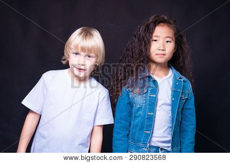 Interracial Children. Two Children Of Caucasian And Asian. Blond Boy And Brunette Girl. On A Blue Ba