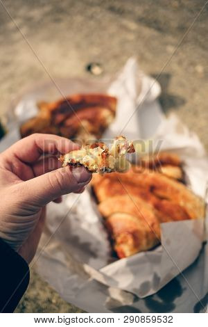 Man Holds A Piece Of Burek With Cheese In His Hand, With Rest Of Burek Blurred In Background On Whit