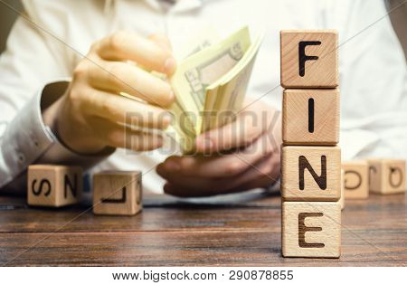 Wooden Blocks With The Word Fine And The Man Calculates The Size Of The Fine. The Concept Of Financi