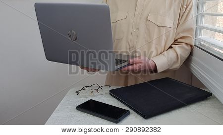 A Man In Light Colored Official Shirt Stands In The Corner Near Window Holds In Hands Open Laptop Co