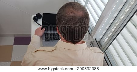 Rear View Of A Man Wearing Official Collar Shirt Sitting Near Window Over Open Laptop Computer Looki