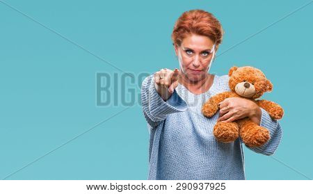 Senior caucasian woman holding teddy bear over isolated background pointing with finger to the camera and to you, hand sign, positive and confident gesture from the front