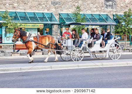 Banff, Canada - July 3, 2011: Tourists On A Horse Drawn Carriage Ride Through Banff Avenue In The Ca