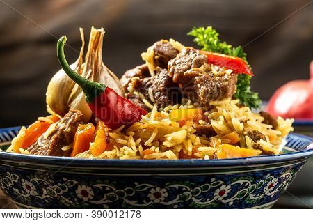 Traditional Uzbek Meal Called Pilaf. Rice With Meat On Plate With Oriental Ornament On A Dark Wooden