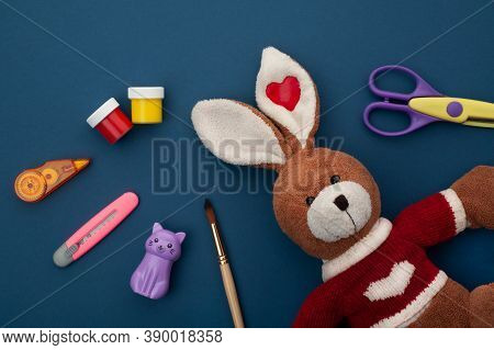 School Supplies Lie On A Blue Background, Next To A Plush Bunny