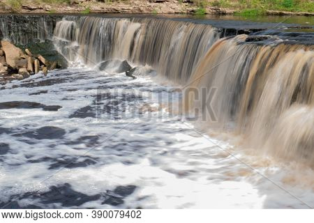 Waterfall, Water Flowing From The River Falls Down. A Stormy River With A Brown Hue.