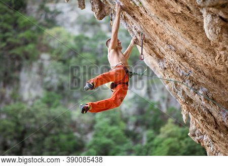 Young Male Rock Climber After Jumping And Gripping Small Handholds On Overhanging Cliff
