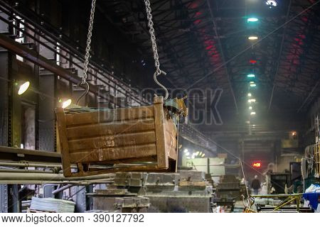 Big Rusty Metal Container Hanging From Chains, Lifted By A Crane Inside The Foundry. Close-up With S