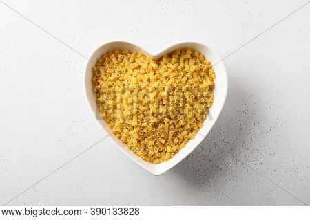 Raw Ditalini Pasta In White Plate In Shape Of Heart On White Background. View From Above.