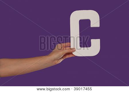 Femelle main tenant jusqu'à la capitale majuscule C isolé contre une vue fond violet