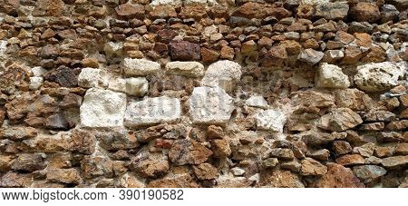 Stone Wall. Stacked Large Bricks And Cobblestones In Warm Colors. Loose White Stones Protruding From