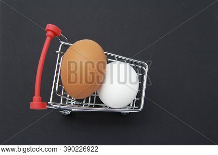 Eggs, Two Chicken Eggs, Brown And White, In A Small Shopping Cart. Mini Cart With Eggs On A Dark Gra