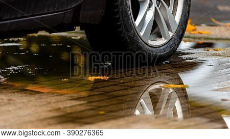 Puddle On The Pavement With A Reflection Of The Car Wheel And Colorful Autumn Leaves