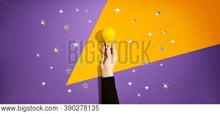 Person Holding A Yellow Light Bulb With Silver Shiny Stars