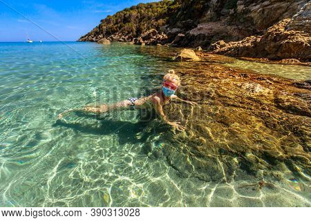 Woman Swimming In Fetovaia Beach And Crystal Sea With A Surgical Mask During Covid-19. Blonde Touris
