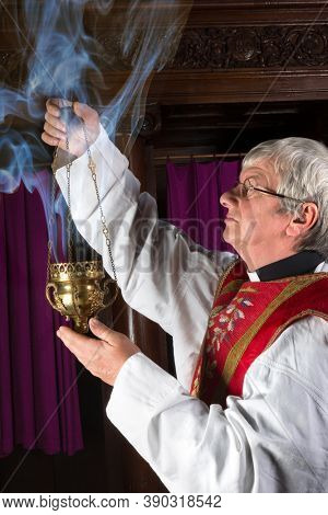 Priest in red chasuble burning incense during mass