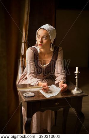Old master style portrait of a young maid in historical costume writing a letter with a feather quill