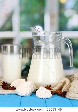 Jarra e copo de leite com merengue em malhas de gola alta na mesa de madeira no fundo da janela