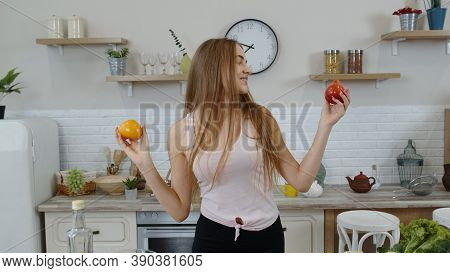 Happy Young Smiling Teen Girl In Kitchen At Home Holding Red And Yellow Tomatoes In Her Hands. Recom